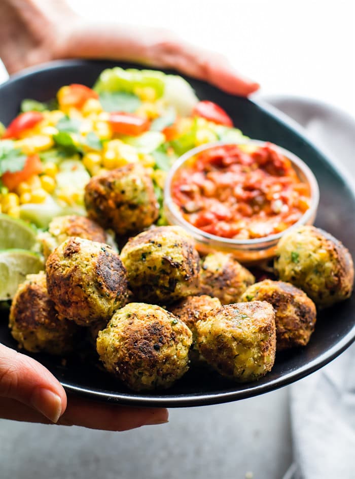 Two hands holding tray filled with Mexican vegan falafel bites and fresh cut vegetables.