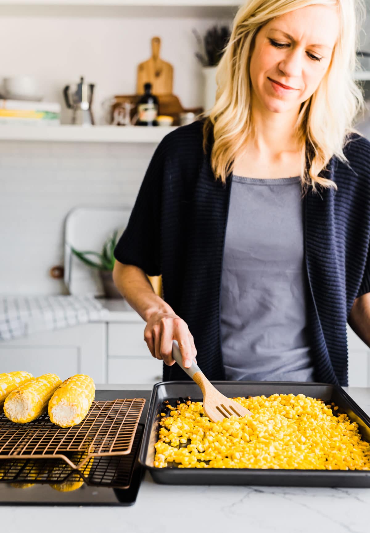 Woman stirring roasted corn kernels on a baking sheet