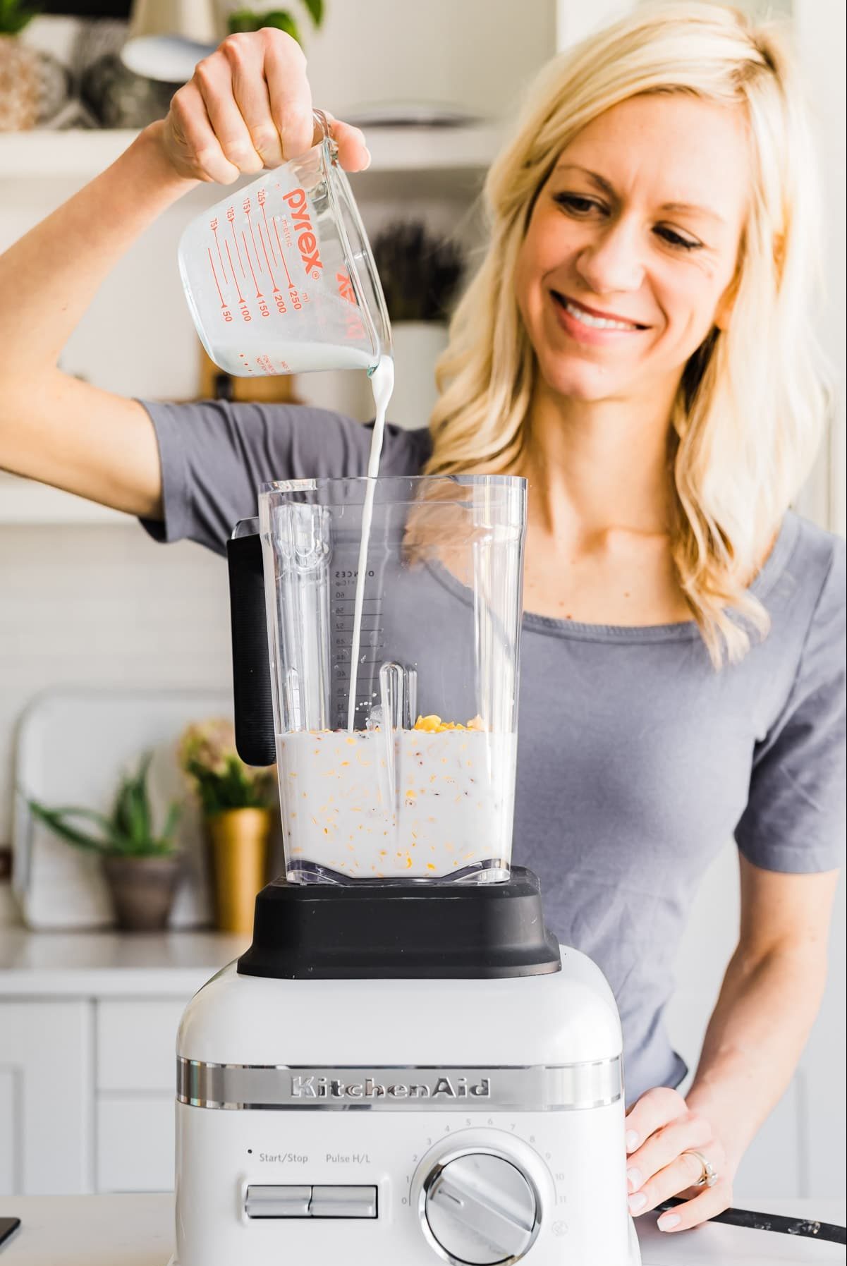 A woman pouring milk from measuring cup into blender for recipe.