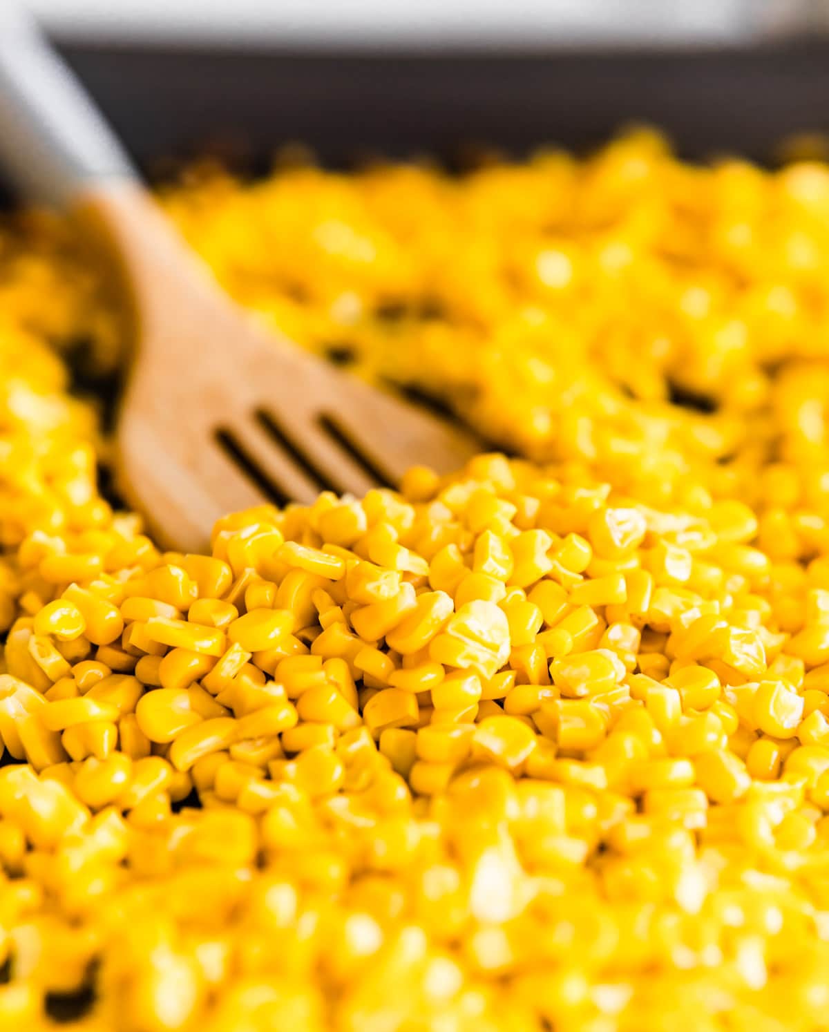 roasted corn kernels being stirred iwth a wooden spatula