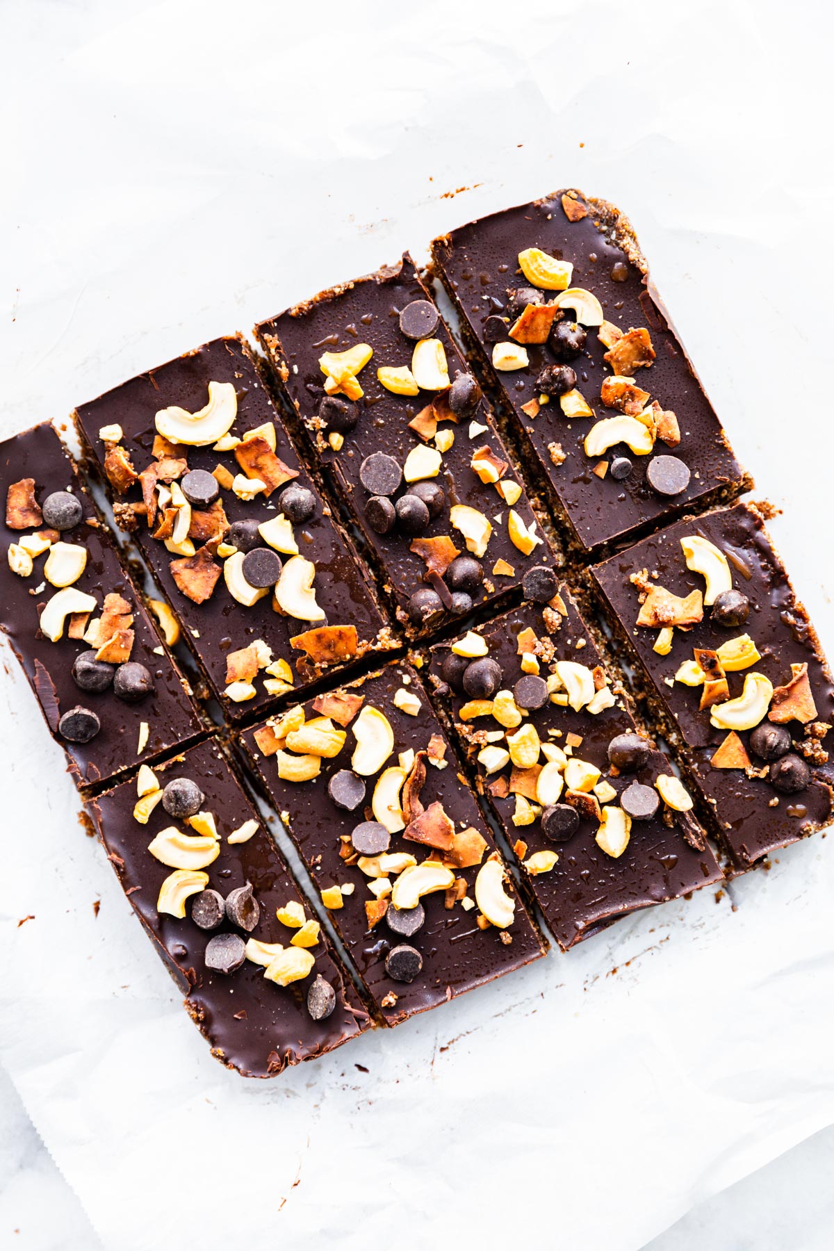 Chocolate cashew fig bars topped with chocolate, cashews, toasted coconut and chocolate chips cut into eight bars.
