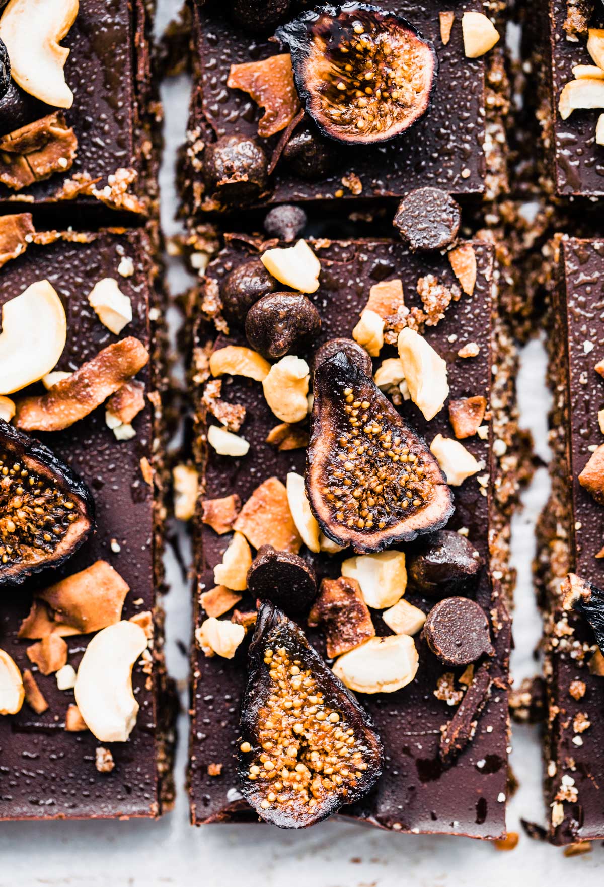 Close up view no bake chocolate cashew fig bars topped with fig pieces, toasted coconut and chocolate chips.