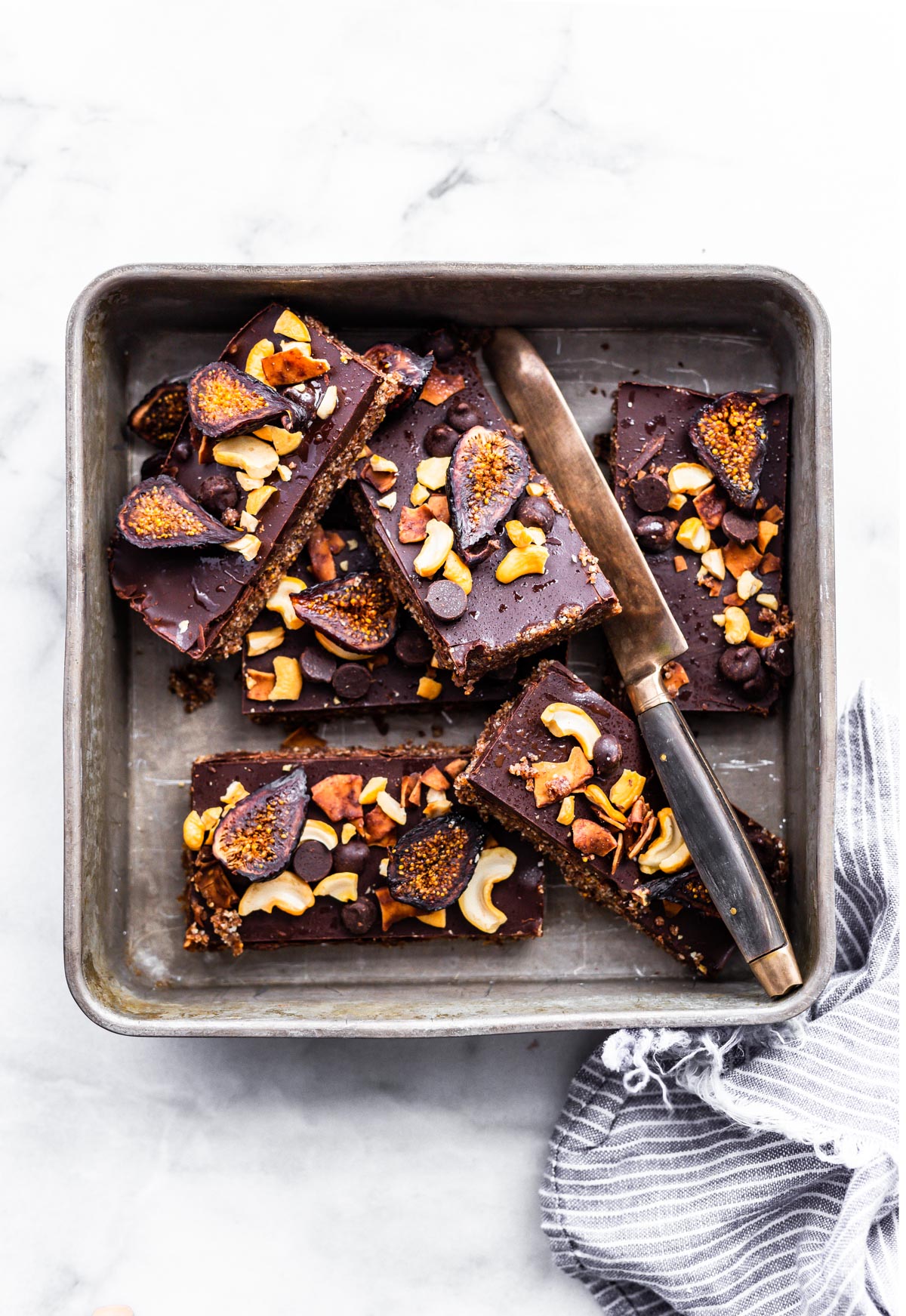 Chocolate cashew fig bars cut into bars arranged in a baking pan with a sharp knife in pan.