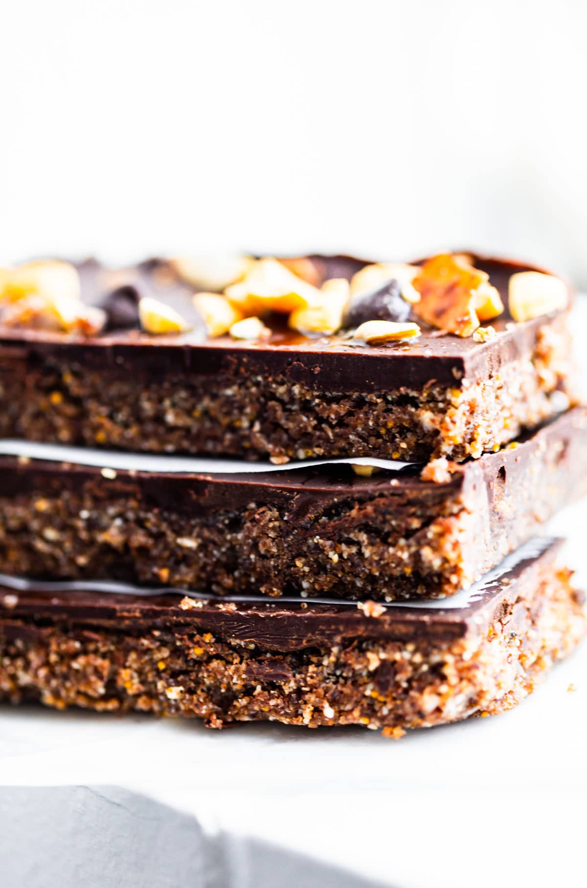 Chocolate topped cashew fig bars stacked up on each other with piece parchment paper between bars.