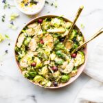 Pink bowl with creamy mustard brussels sprouts salad with a few cranberries in salad.