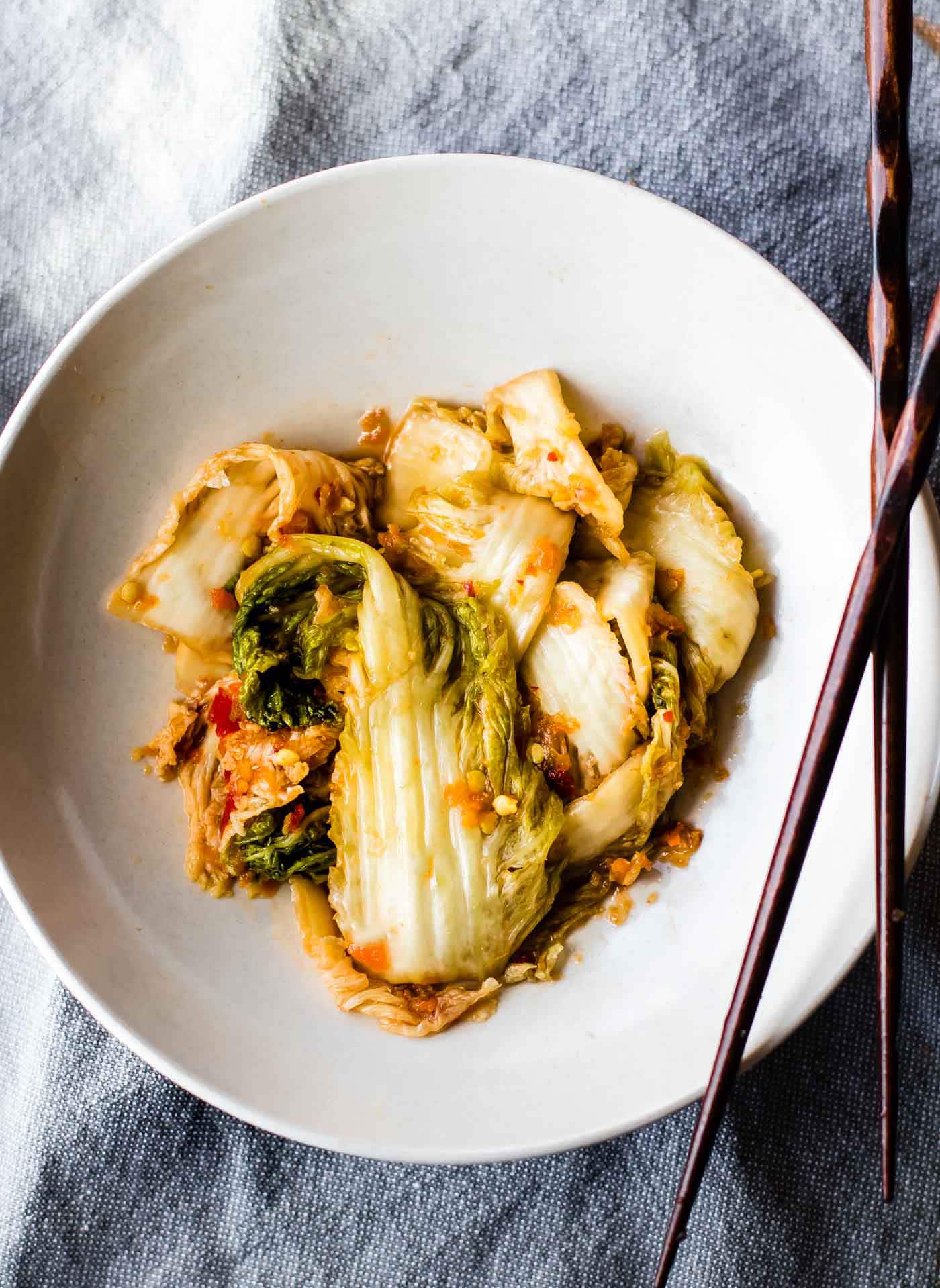 Easy homemade kimchi with red pepper flakes plated on a shallow bowl with chopsticks on the side.