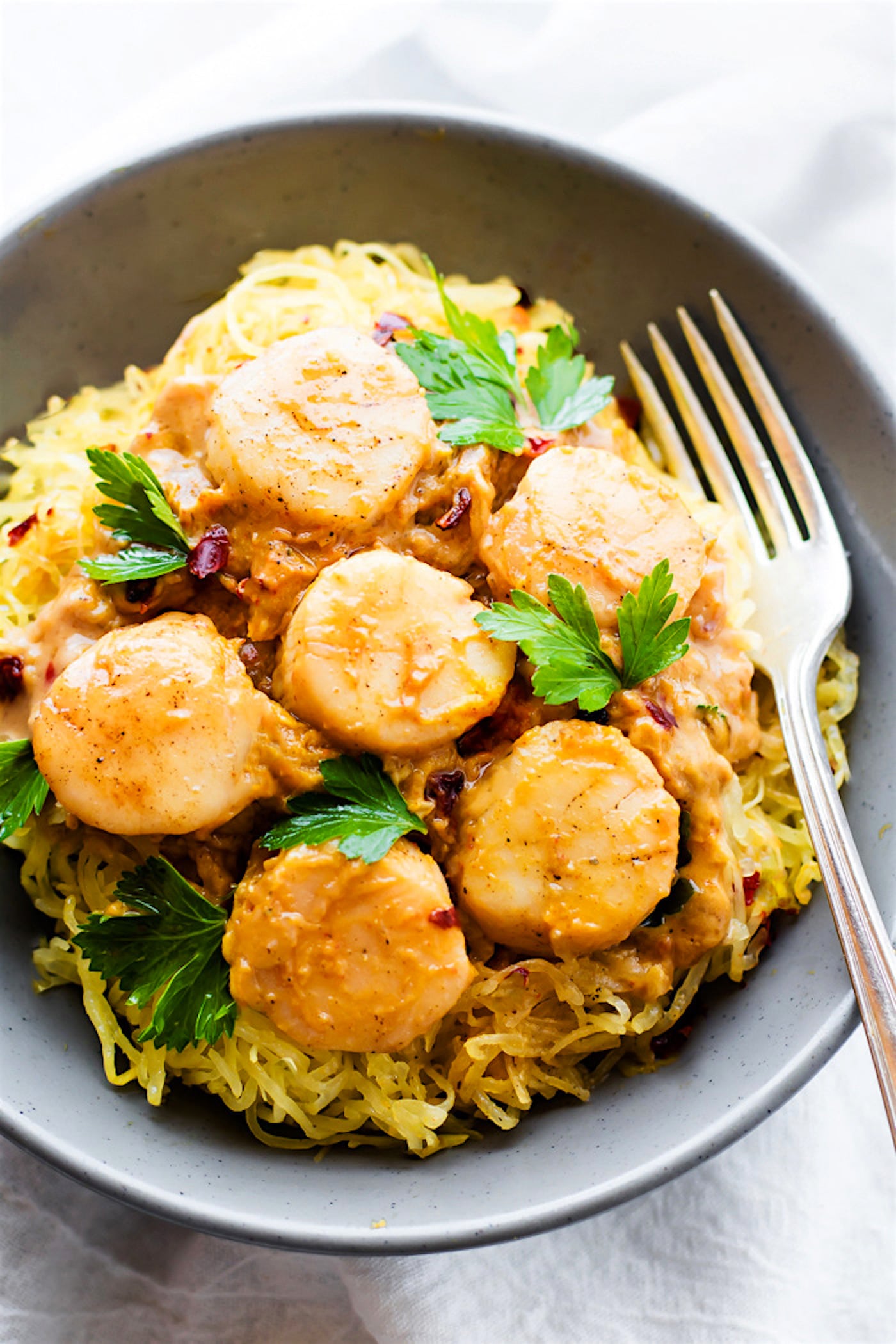 Miso pumpkin coasted scallops over a bed of spaghetti squash pasta served in a grey bowl and topped with fresh herbs.