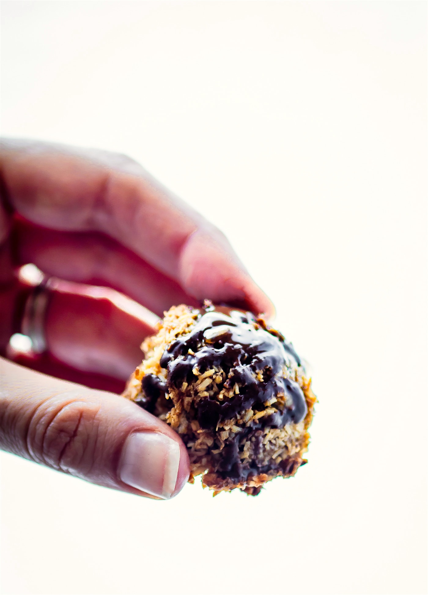 A coconut macaroon with dark chocolate drizzle being held up to show thick texture and hardened chocolate drizzle.