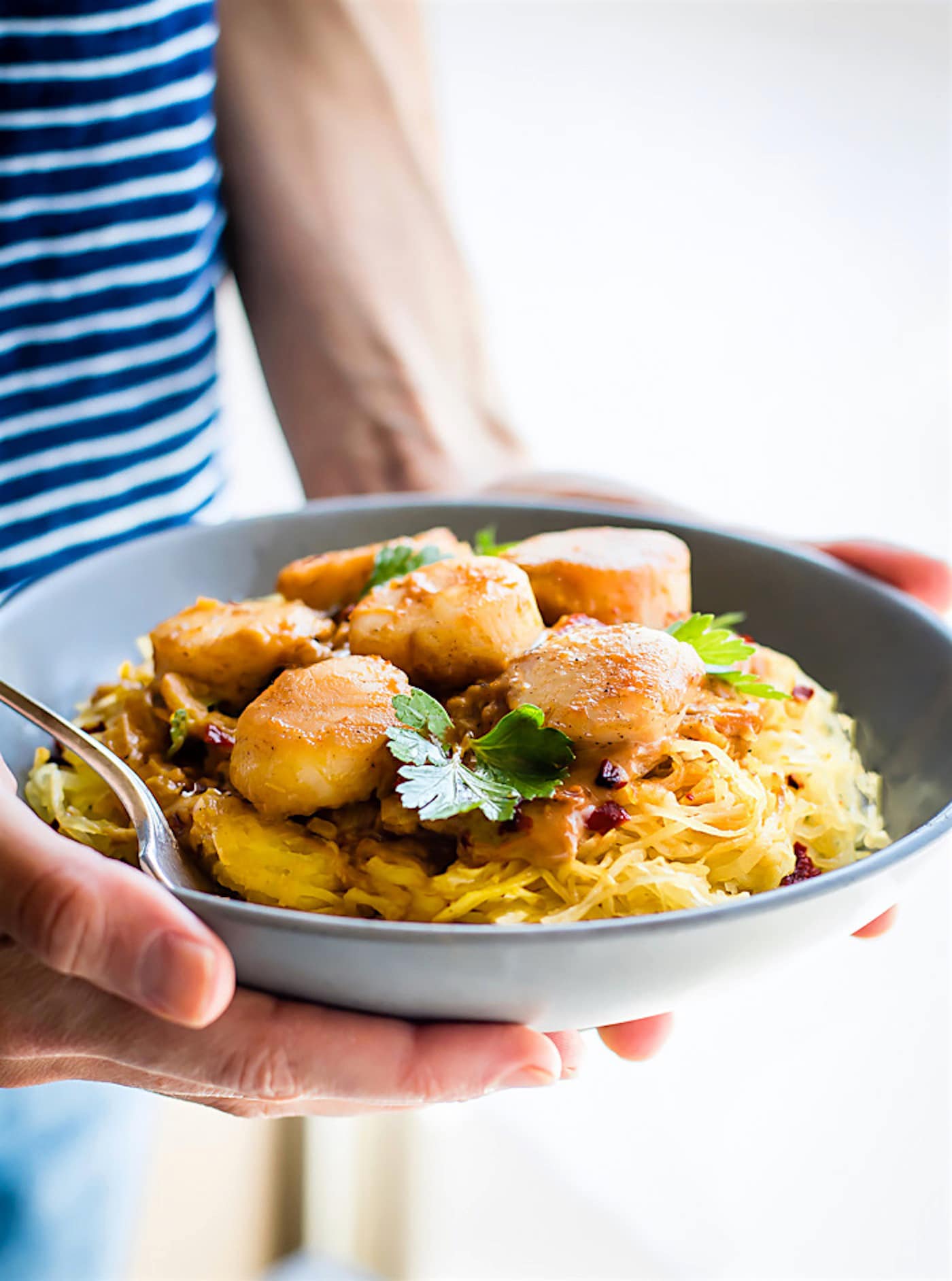 A grey serving bowl of pumpkin spaghetti squash with scallops being held.