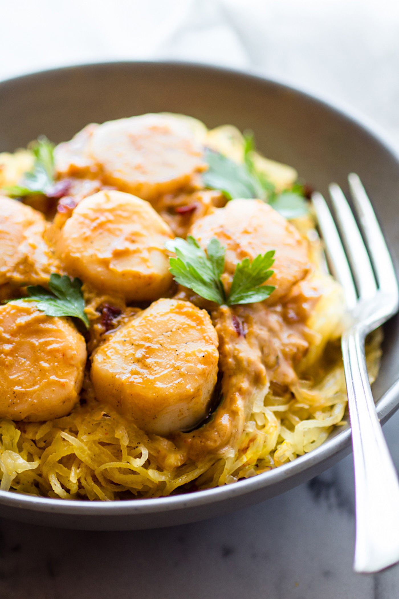 Close up view of miso pumpkin sauce coated scallops over spaghetti squash with fresh herbs.