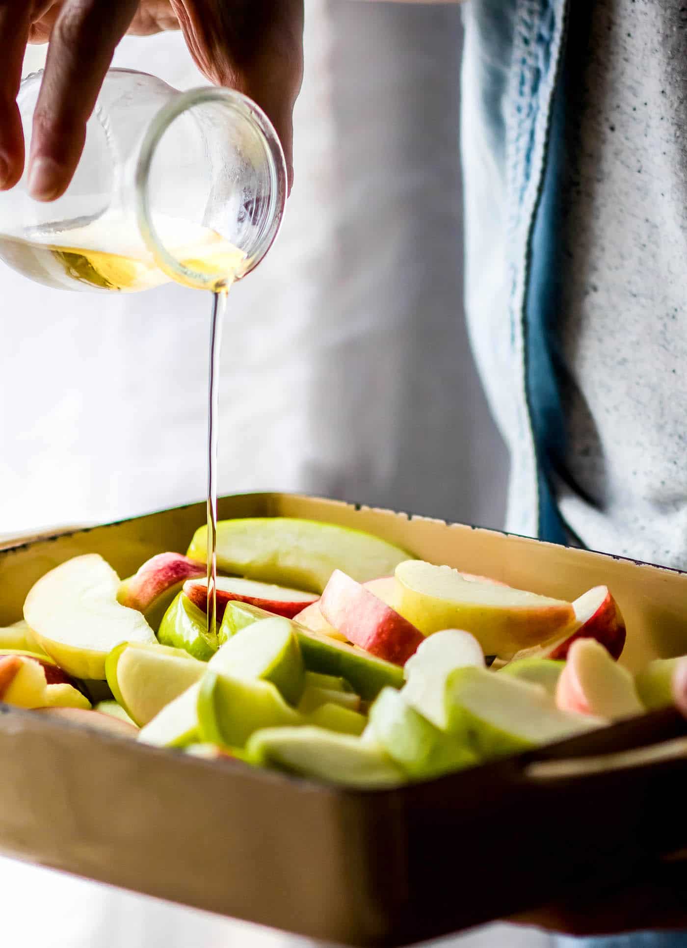 pouring butter and sugar mixture over fresh apple slices before baking in casserole dish.