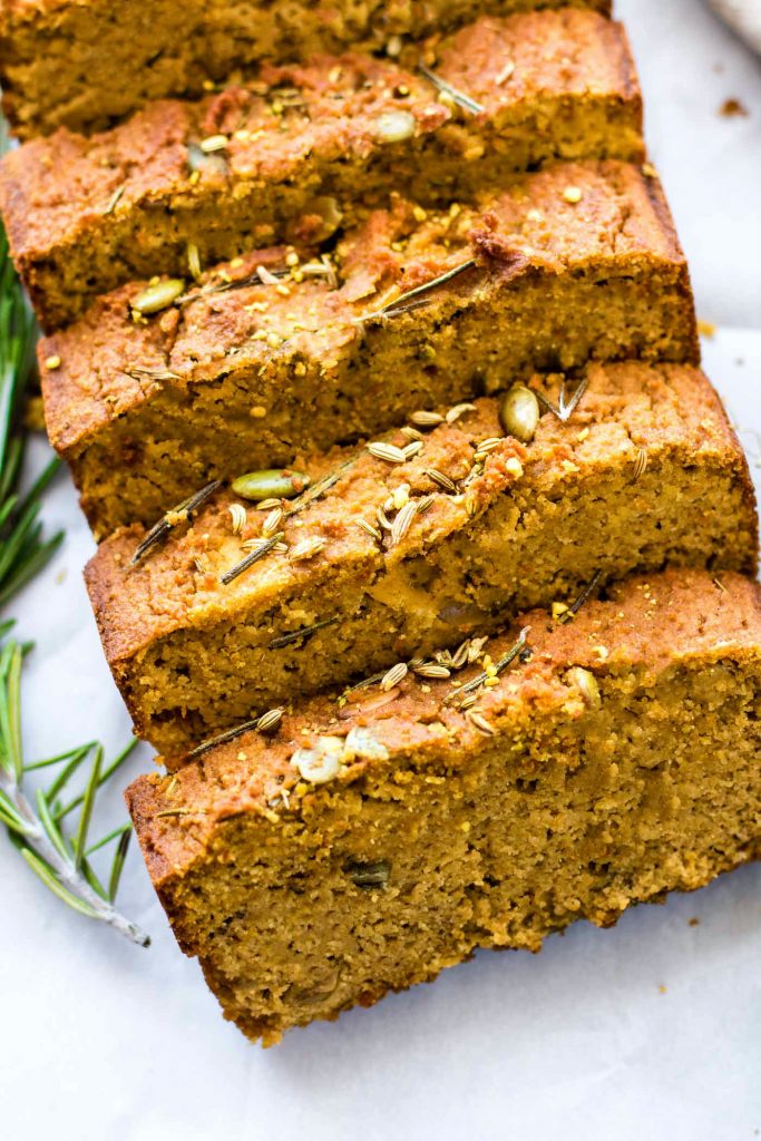 Paleo Pumpkin Rosemary Bread cut into thick slices on white cutting board.