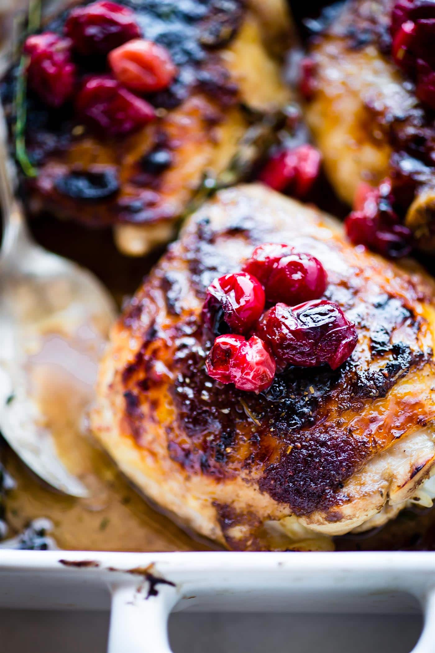 close up image of roasted chicken thighs with fresh roasted cranberries on top
