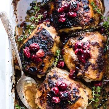 overhead photo: cranberry balsamic chicken on a baking sheet with serving spoon
