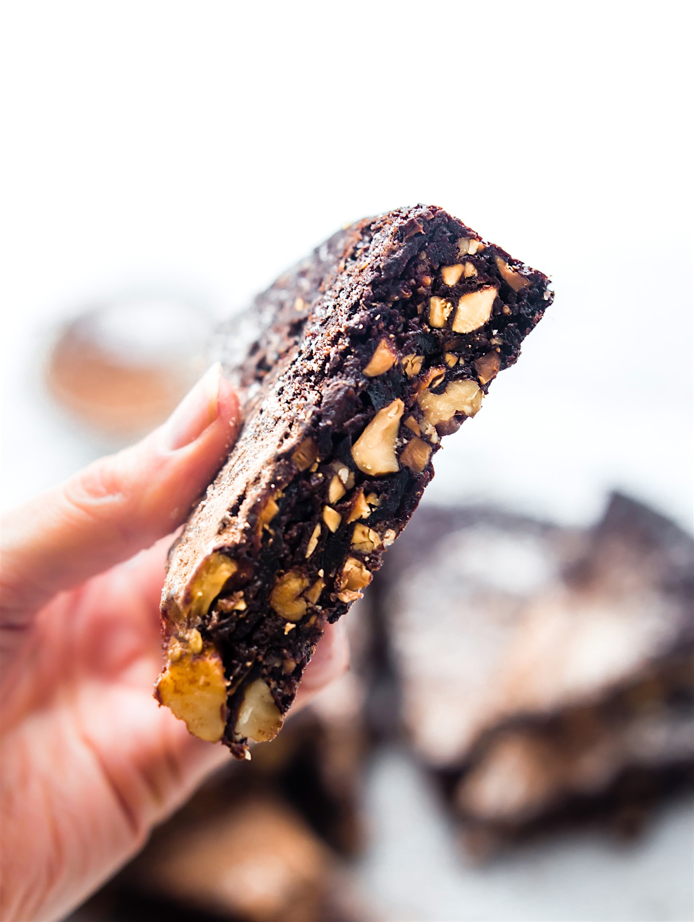 A hand holding a slice of chocolate Christmas cake with nuts