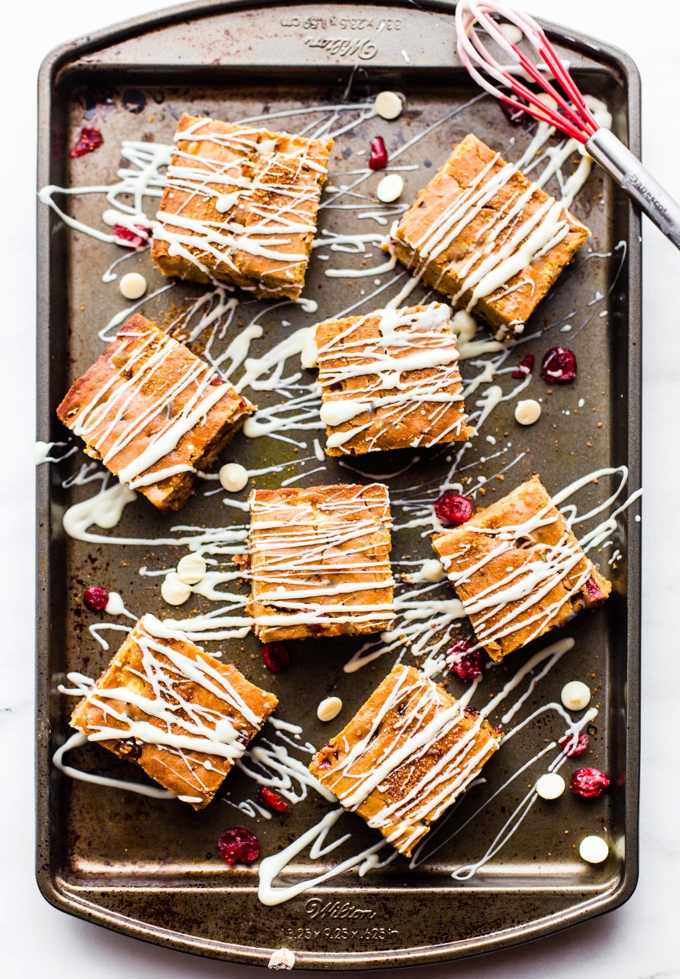 Vegan cranberry white chocolate pumpkin bars on a baking sheet, drizzled with white chocolate