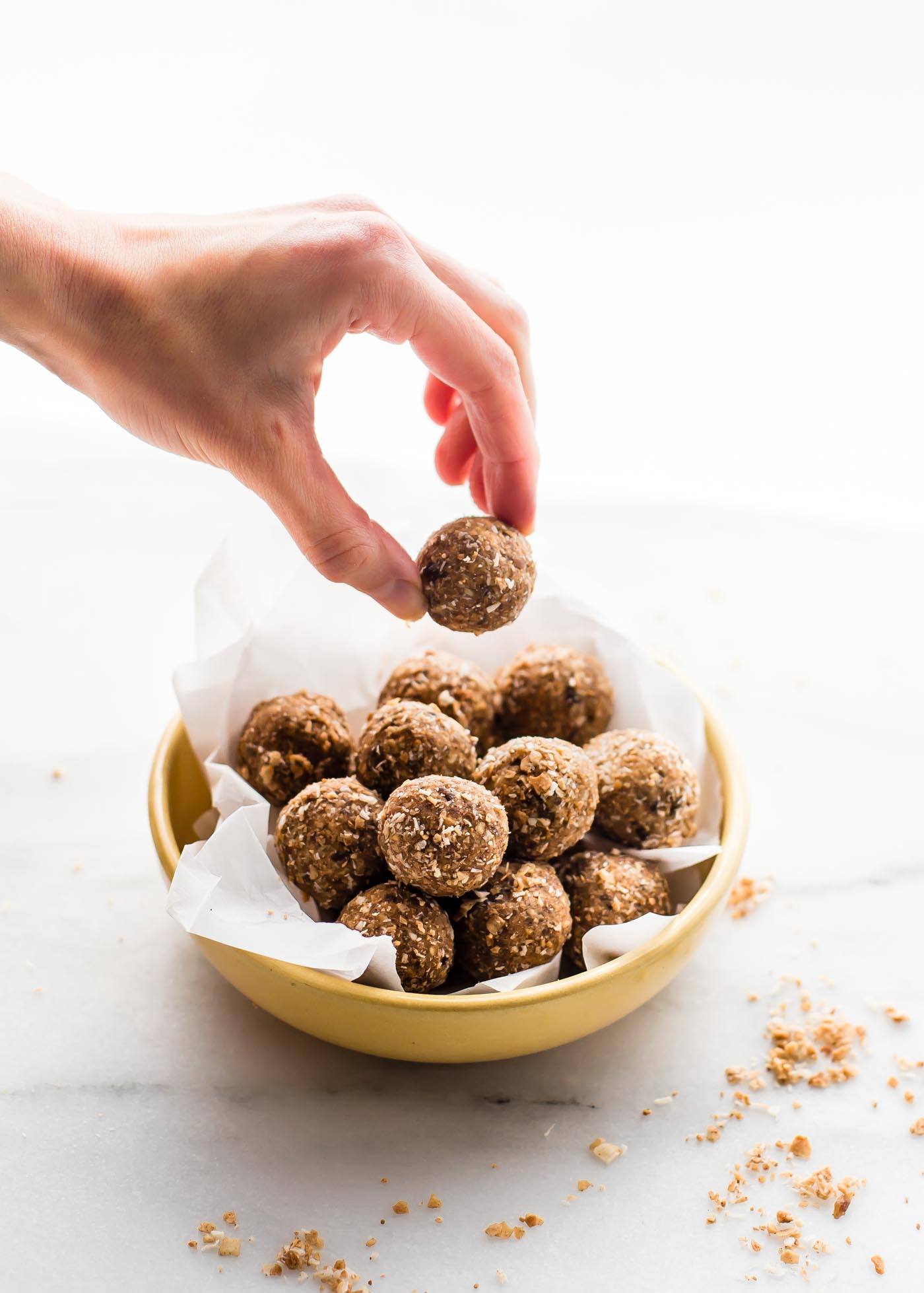 bowl of Cinnamon Toasted Coconut Bliss Balls - a hand holding one of them