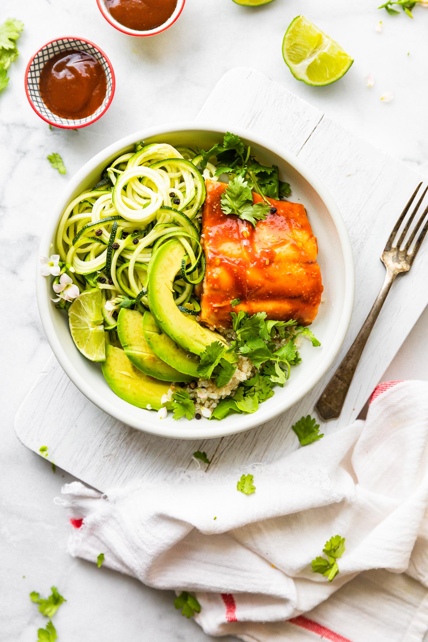 BBQ baked salmon and avocado and zucchini in shallow white bowl on white cutting board.