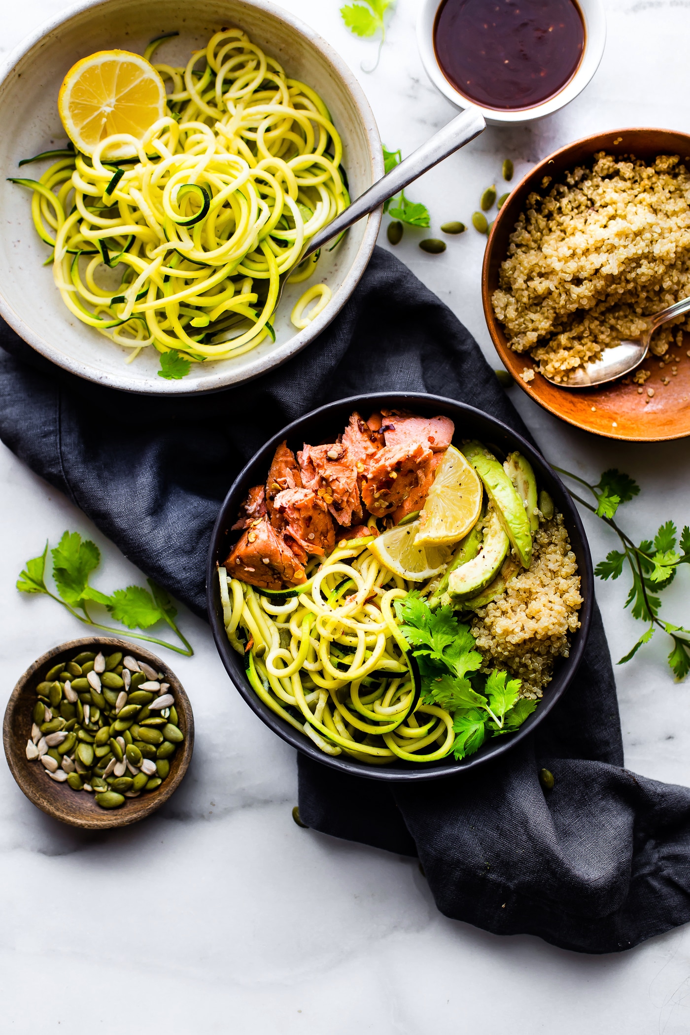 Black bowl filled with quinoa, bbq baked salmon, zucchini noodles and avocado slices