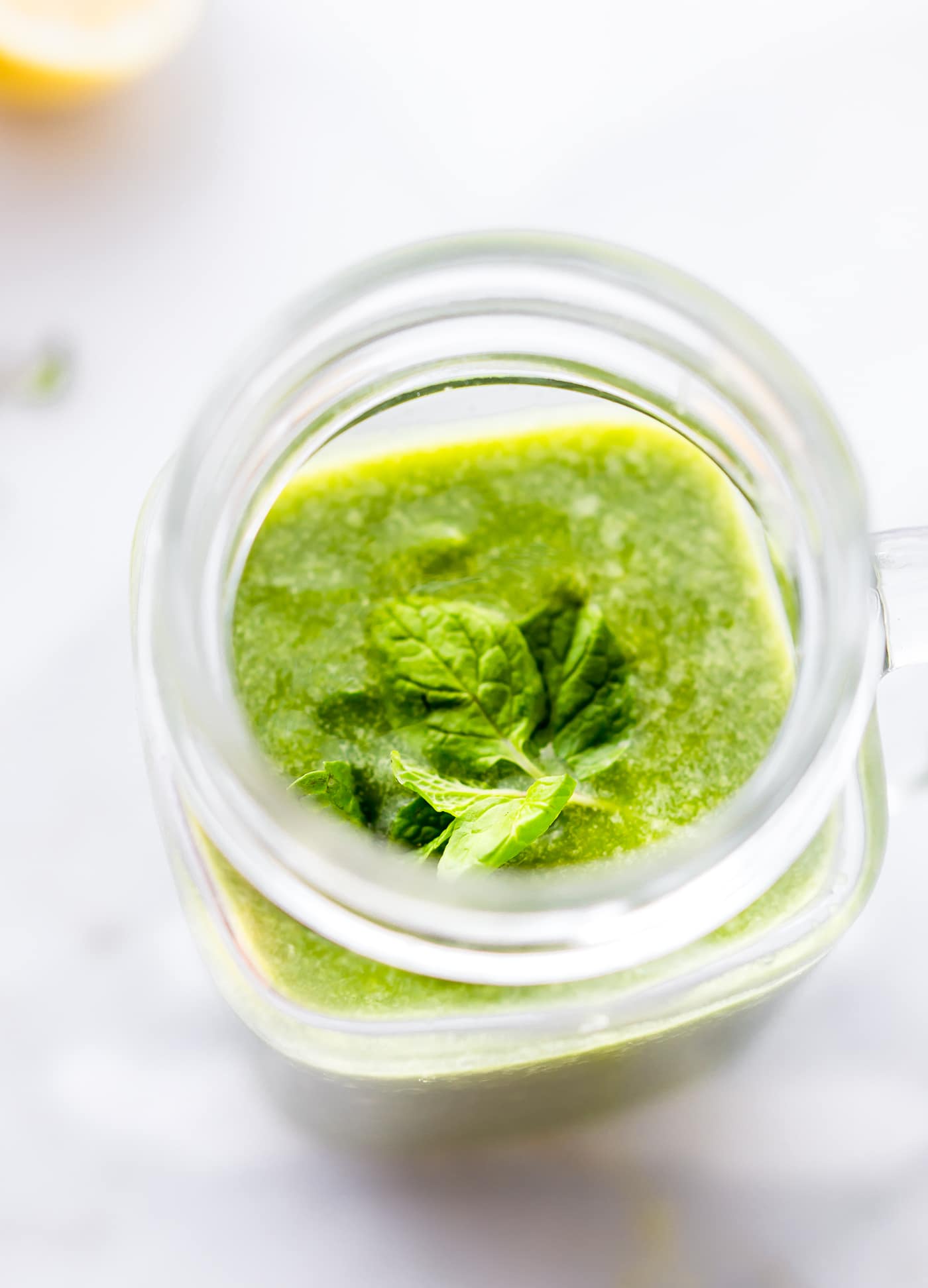 Looking into glass cup filled with green smoothie topped with sprig of mint.