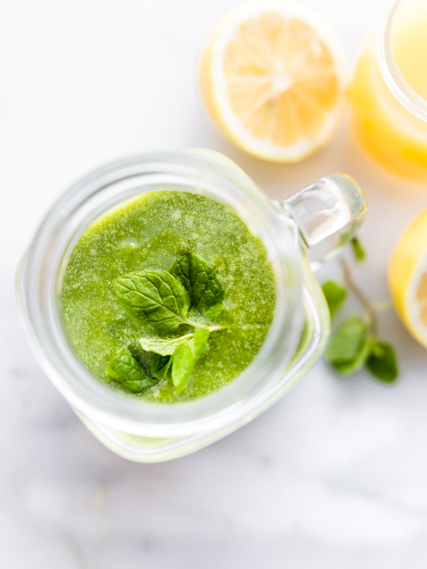 Looking into mason jar cup filled with bright green smoothie with sprig of fresh mint on top.