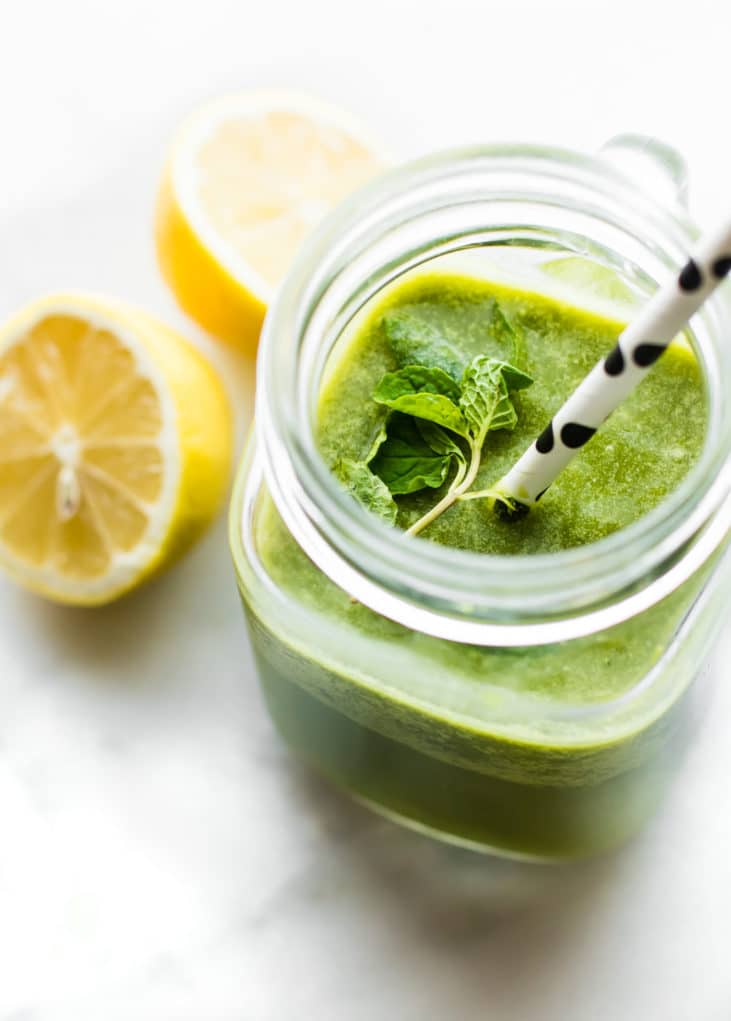 Overhead view green smoothie in mason jar cup topped with fresh mint and polka dot straw