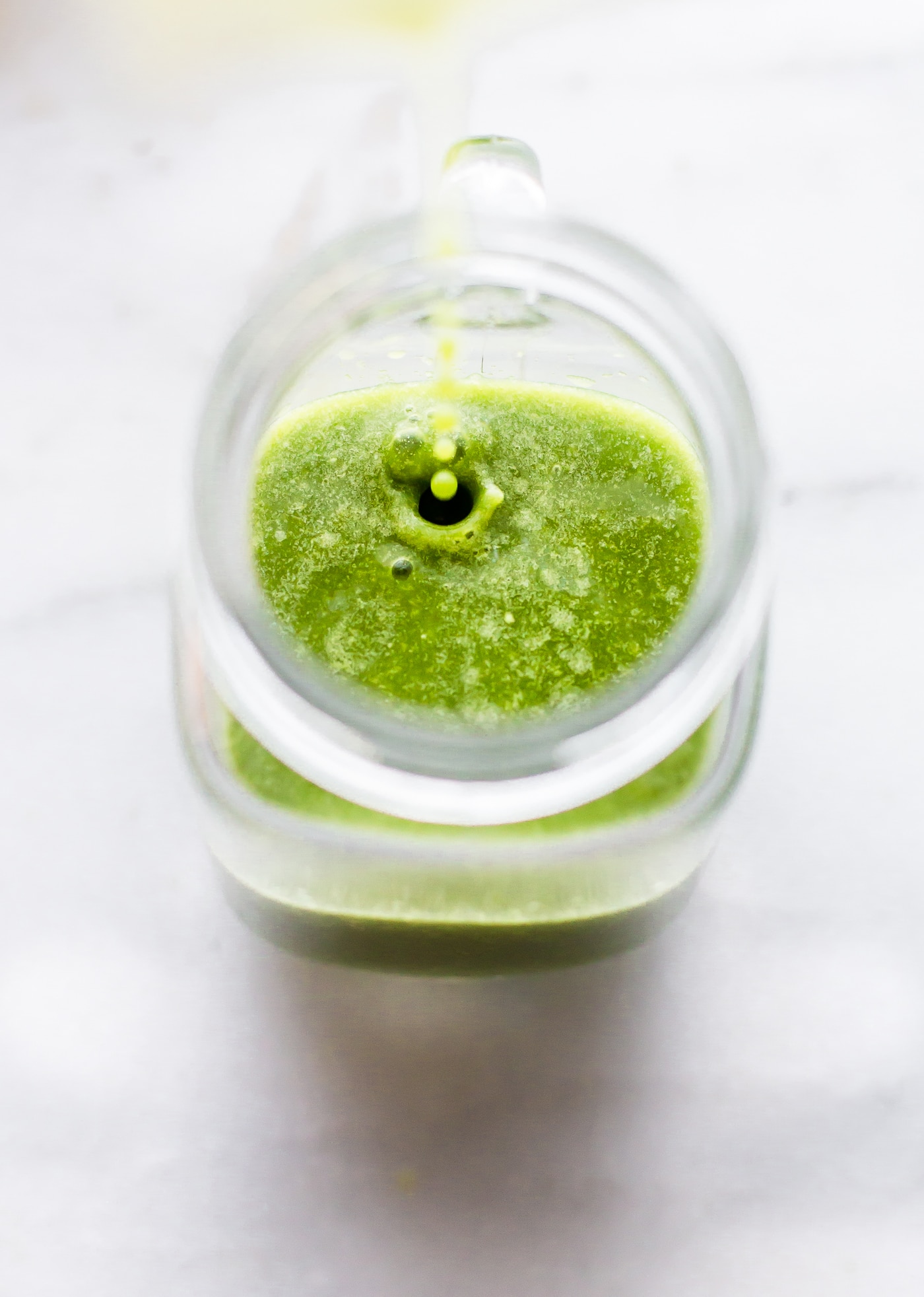 Bright green power smoothie being poured into a glass cup