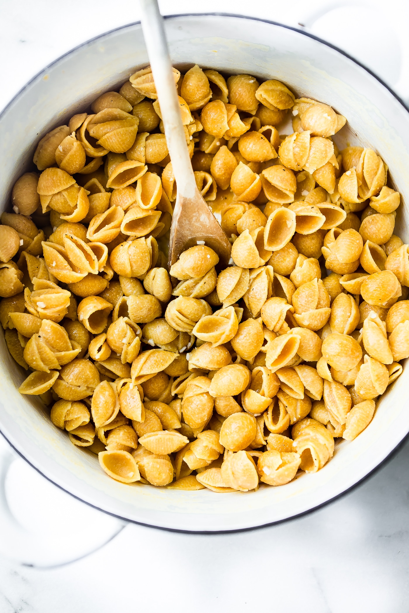 Overhead view cooked pasta mini shells in white bowl with wooden spoon.