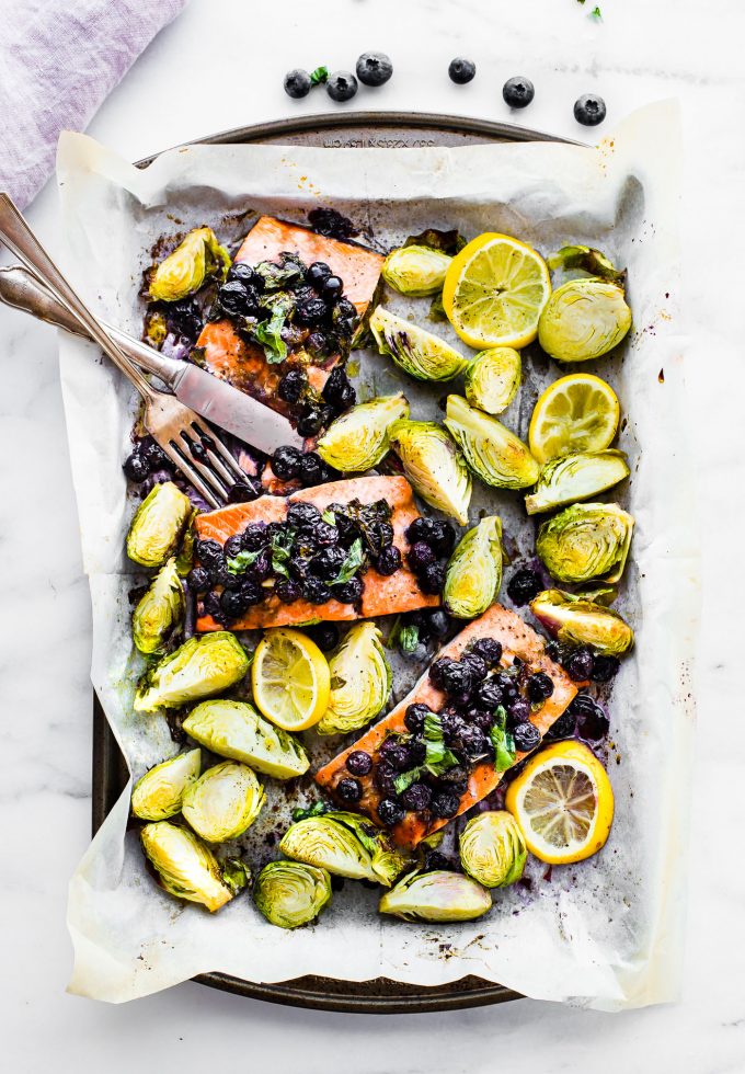 One pan superfood salmon on parchment lined baking sheet with roasted Brussels sprouts and lemon wedges.