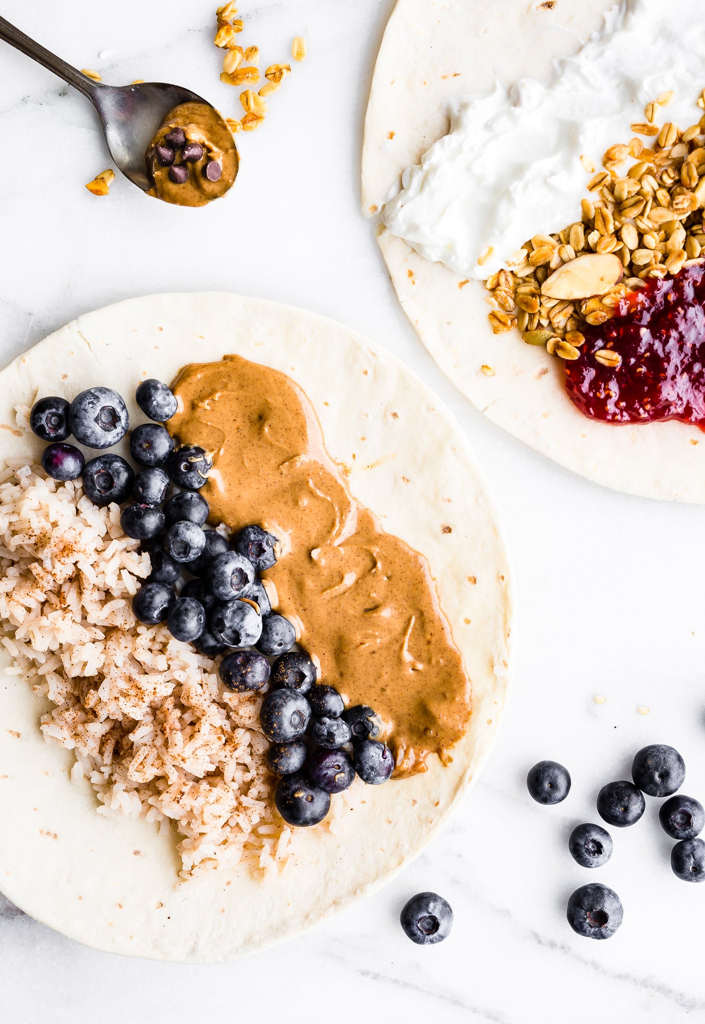 overhead image of large corn tortilla covered with nut butter, cooked brown rice, cooked oats, and blueberries