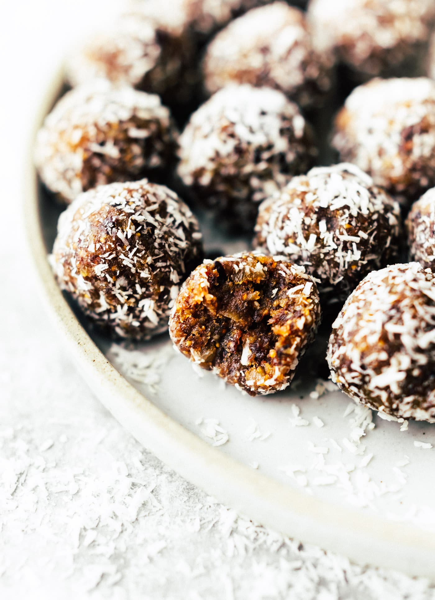 plate of No Bake Coconut Apricot Fig Bliss balls, energy bites with a bite taken out of one ball and coconut shreds all around the plate