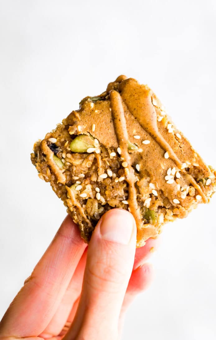 maple sesame quinoa bar topped with nut butter being held between thumb and forefinger
