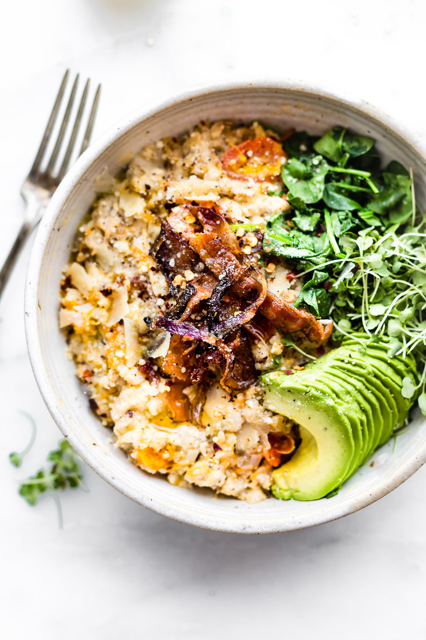 Close up overhead view savory slow cooker oatmeal in bowl topped with crispy bacon, micro greens, and sliced avocado.