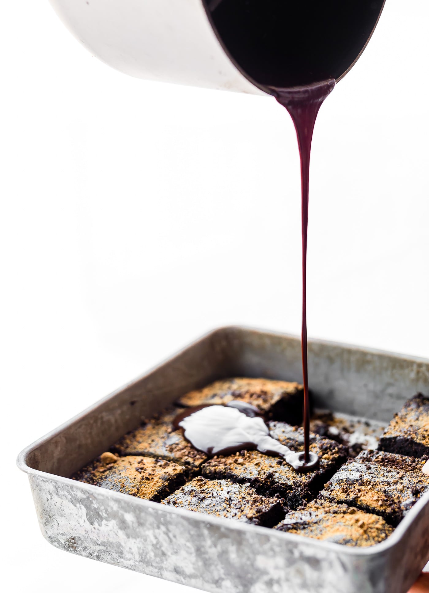 Dark chocolate being poured over dirty chai dark chocolate flourless brownies in metal pan
