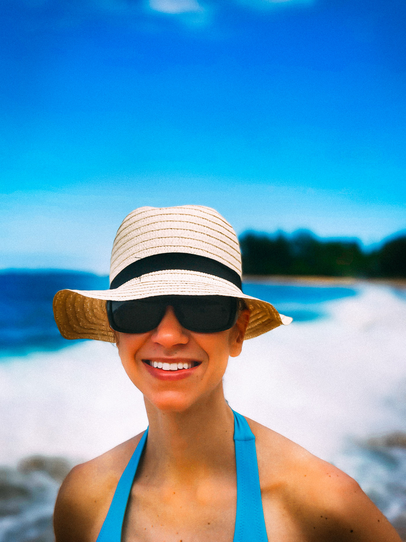 A woman wearing blue swimsuit, sunglasses, and hat on the beach.