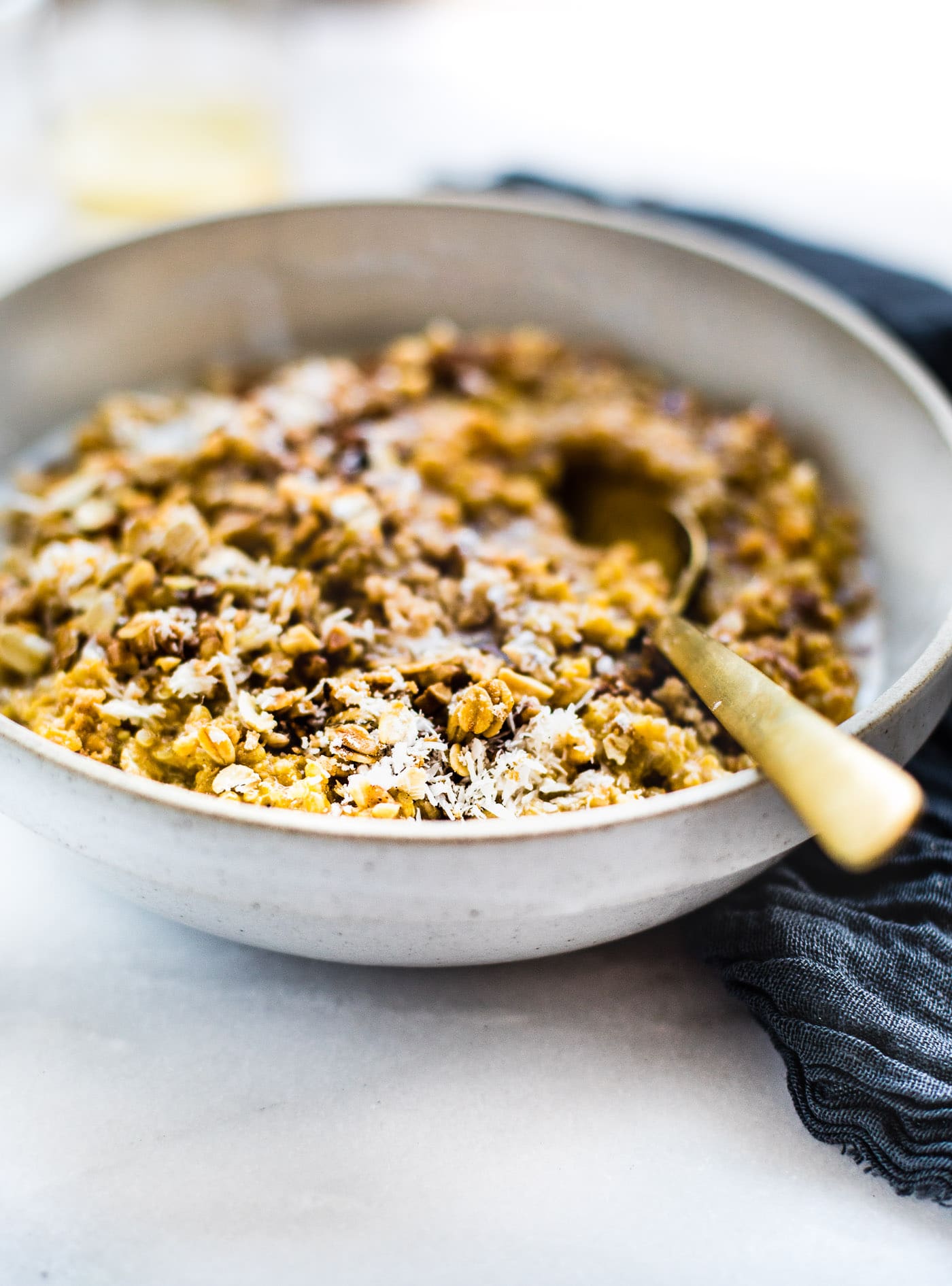 Side view creamy vegan pumpkin quinoa breakfast in stone bowl with gold spoon.