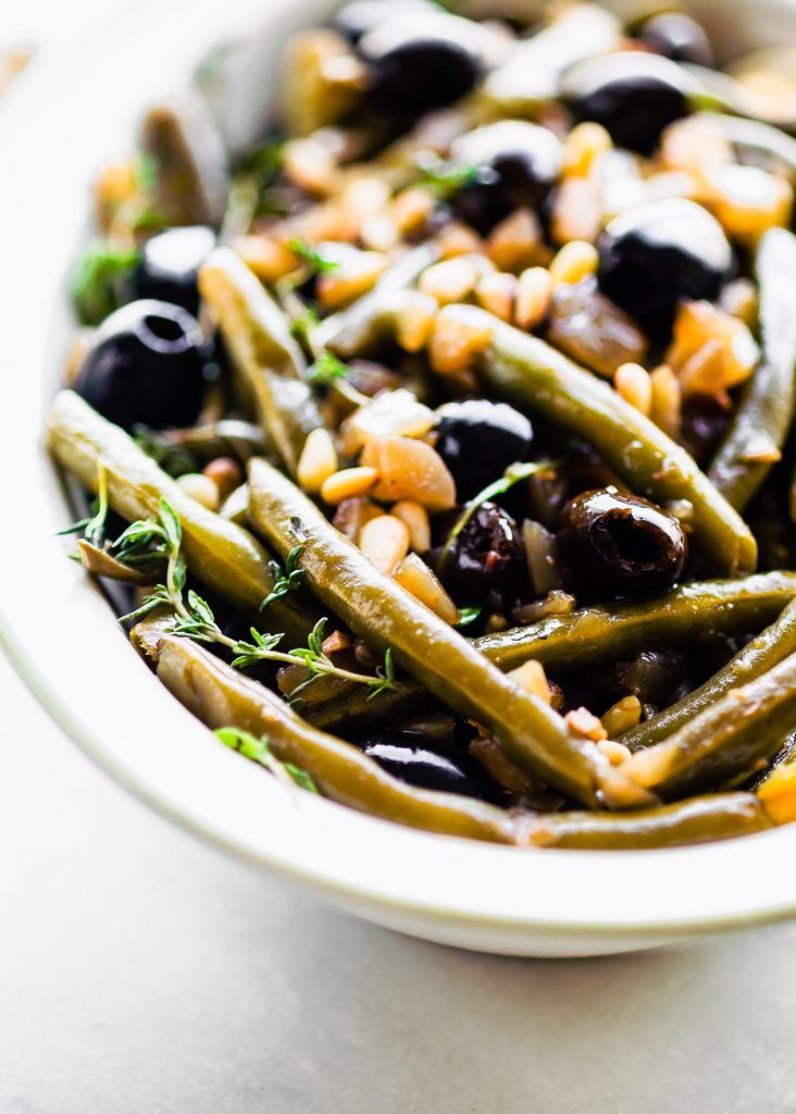 Close up view balsamic olive oil braised green beans and olives in serving dish.
