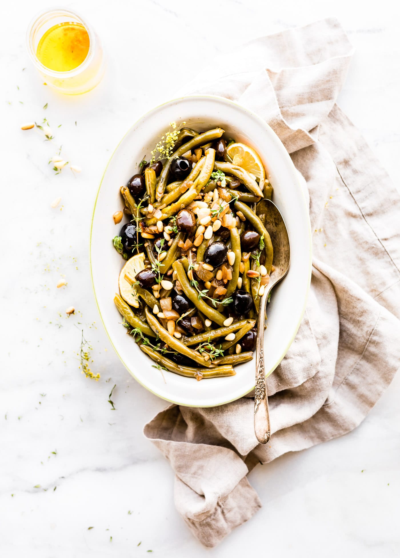Balsamic Olive-Oil braised green Beans with a quick, easy, and healthy side dish. For this braised green beans recipe, fresh green beans are seasoned with thyme, then braised with balsamic vinegar, olive-oil, onion, black olives, and topped with toasted pine nuts. Paleo, whole 30, and vegan friendly.