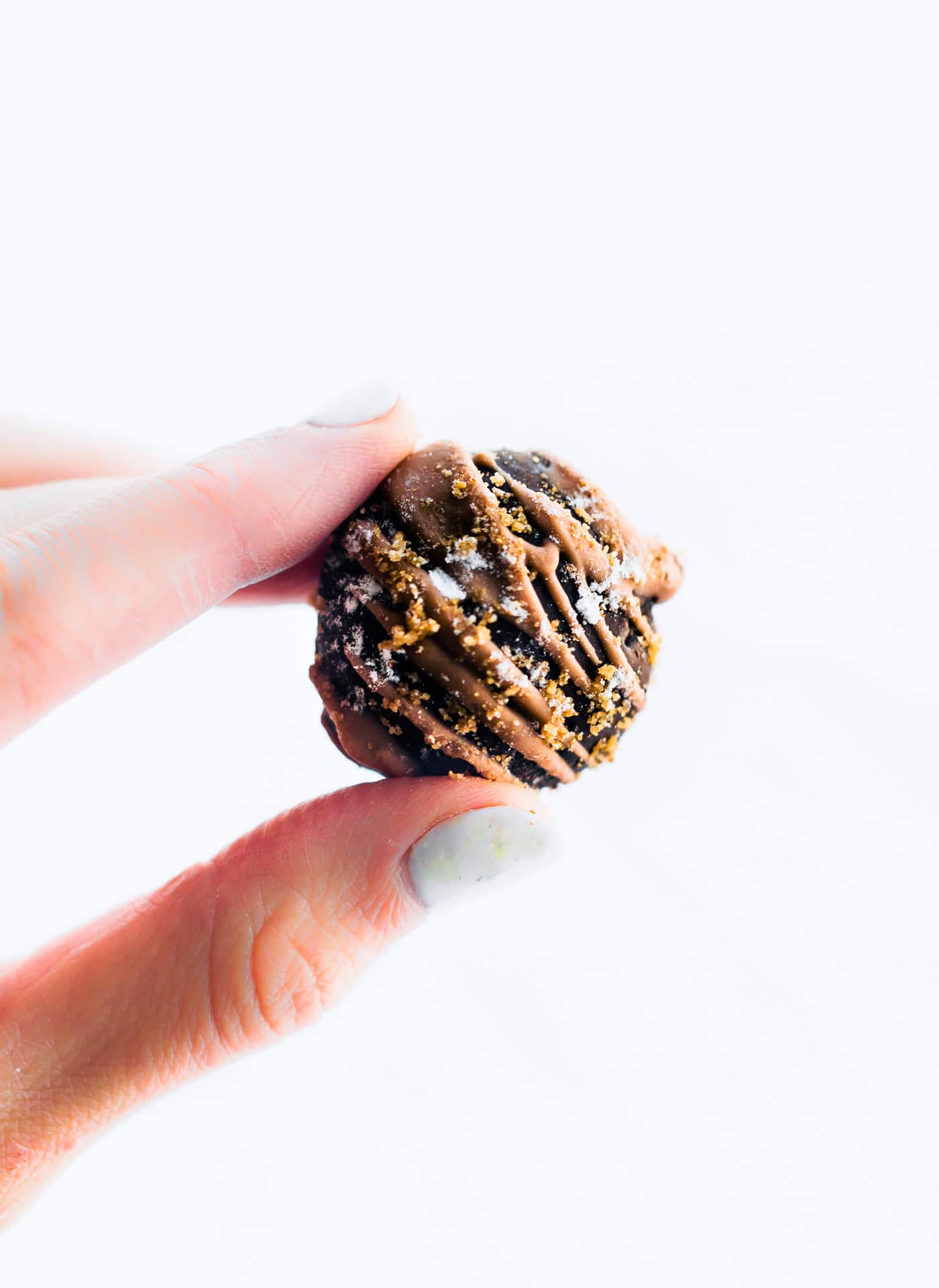 A single dark chocolate amaretto cake bite drizzled with almond butter and dark chocolate being held between thumb and forefinger.