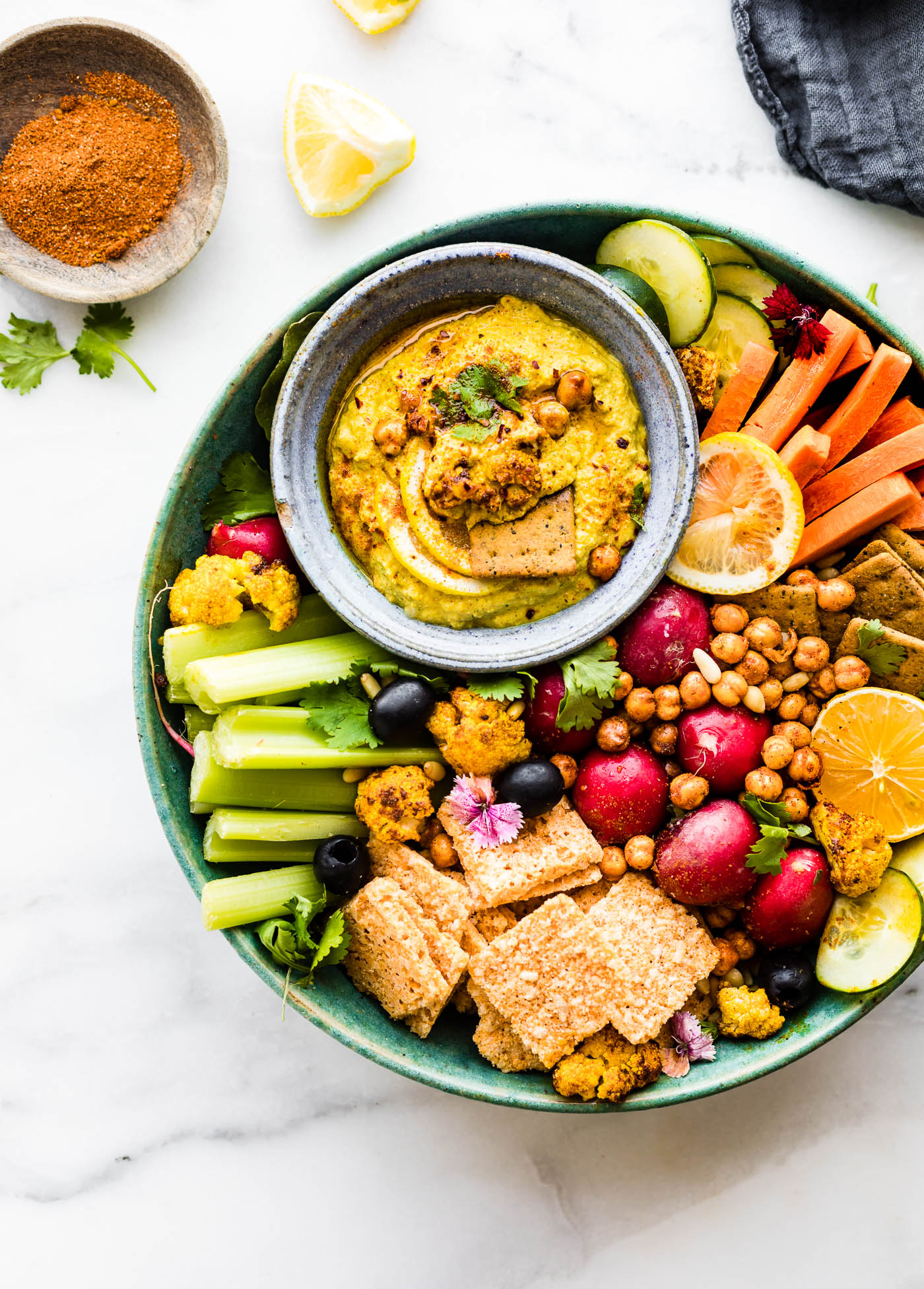 Tandoori Roasted Cauliflower dip in gray stone bowl on turquoise stone tray filled with vegetables and chickpeas.