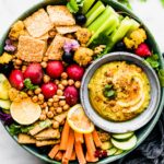 Turquoise tray filled with cut vegetables and crackers, grey bowl filled with Tandoori roasted cauliflower dip on tray.