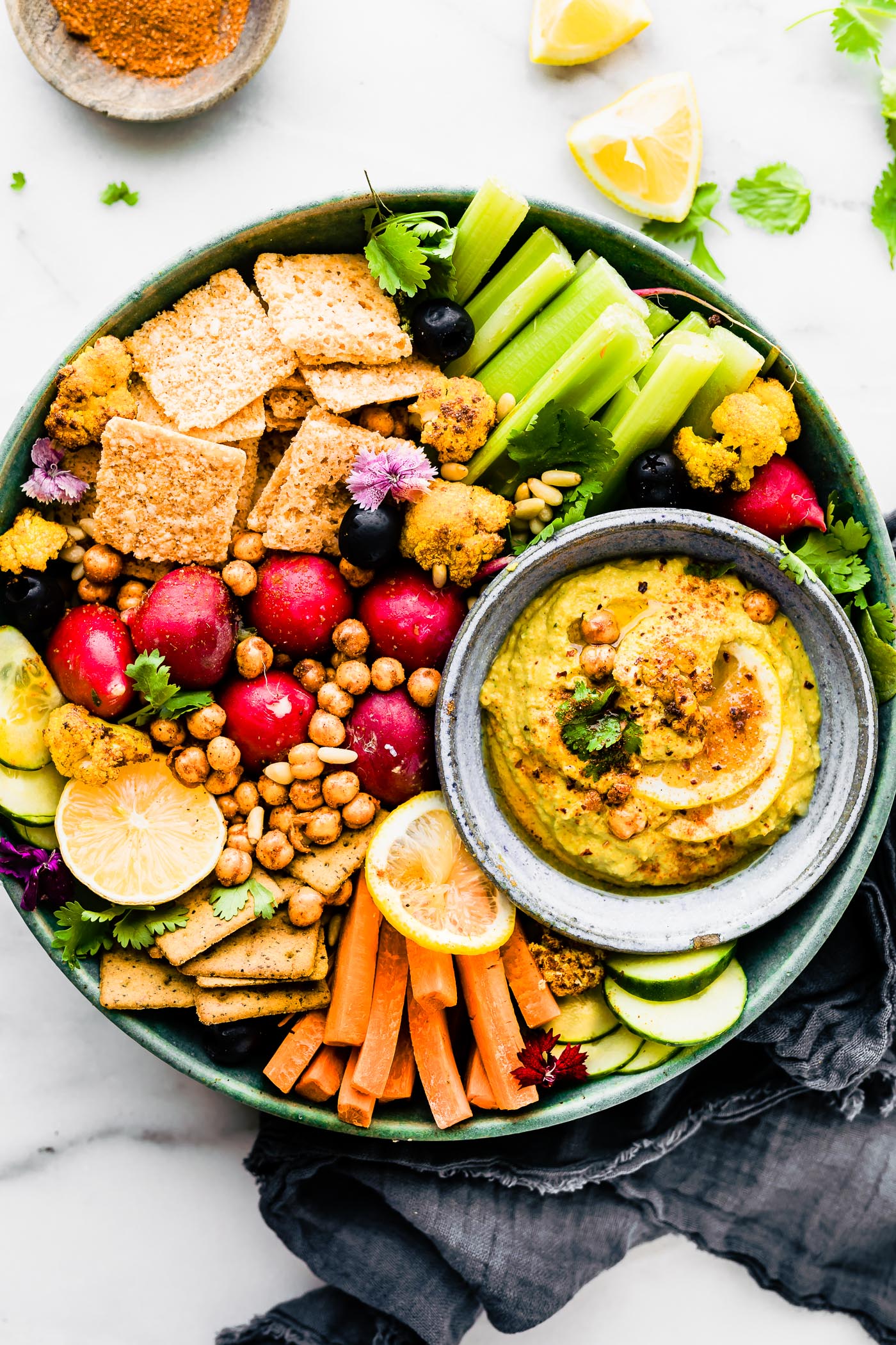 Overhead view turquoise tray filled with crackers and vegetables, grey stone bowl filled with Tandoori roasted cauliflower dip.
