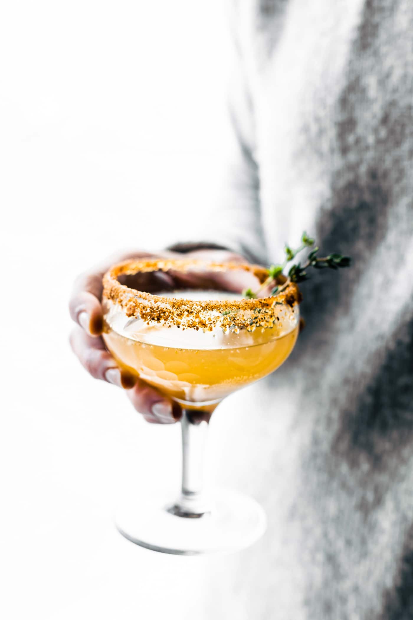 A glass of honey roasted pear cocktail with sugared edge being held by hand.