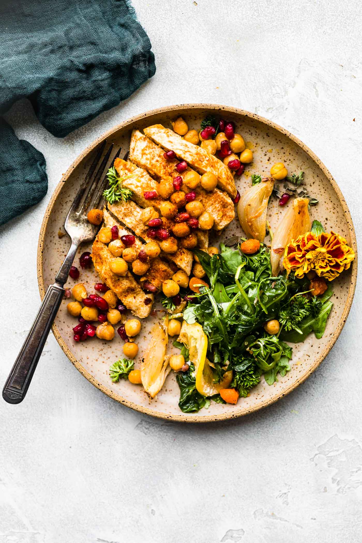 Overhead view cumin roasted chickpea chicken cut into strips topped with chickpeas and pomegranates in a turquoise bowl