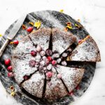 Overhead view cranberry sour cream almond round cake topped with sugared cranberries and powdered sugar.