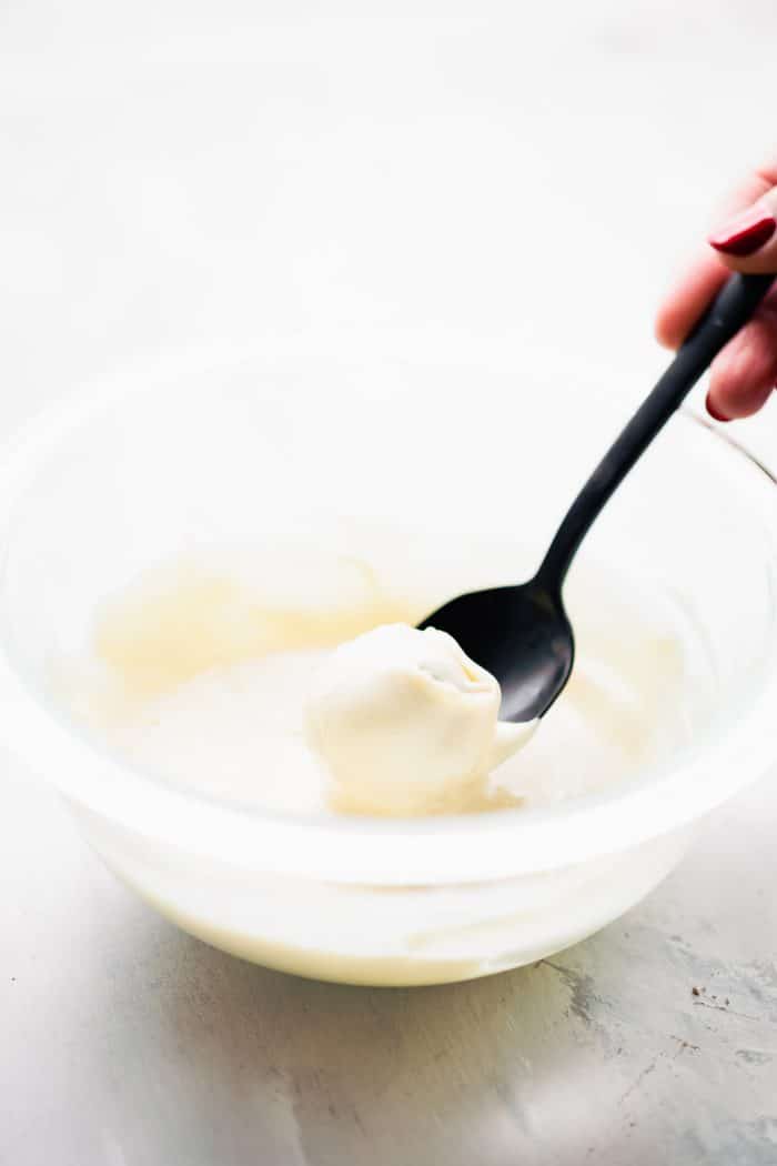 A black spoon scooping up melted white chocolate from a bowl