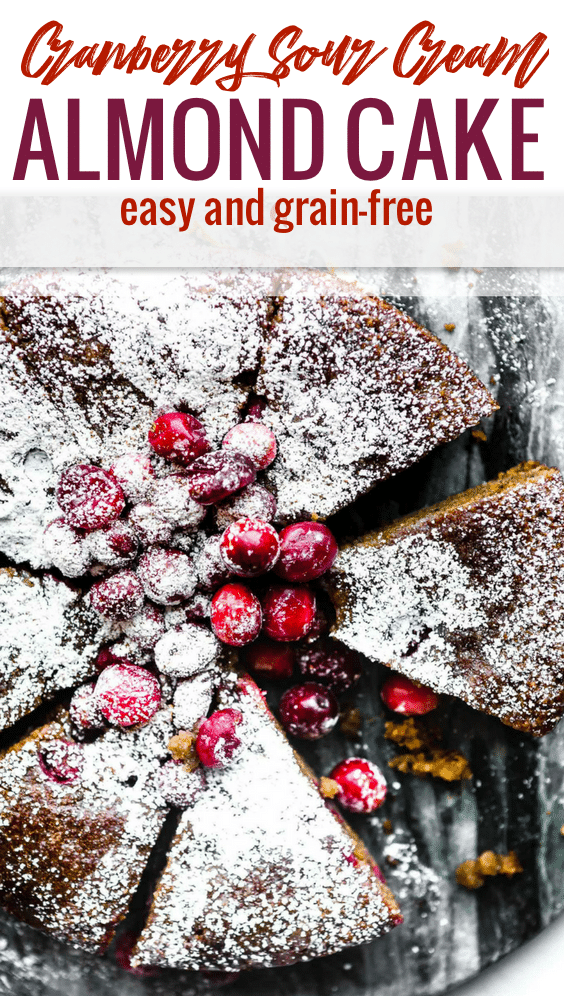 Close up overhead view cranberry sour cream almond cake cut into slices topped with sugared cranberries and powdered sugar.