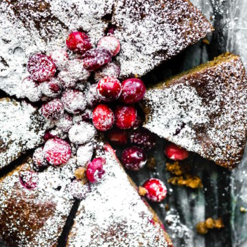 Cranberry Sour Cream Almond Cake cut into slices topped with sugared cranberries and powdered sugar.