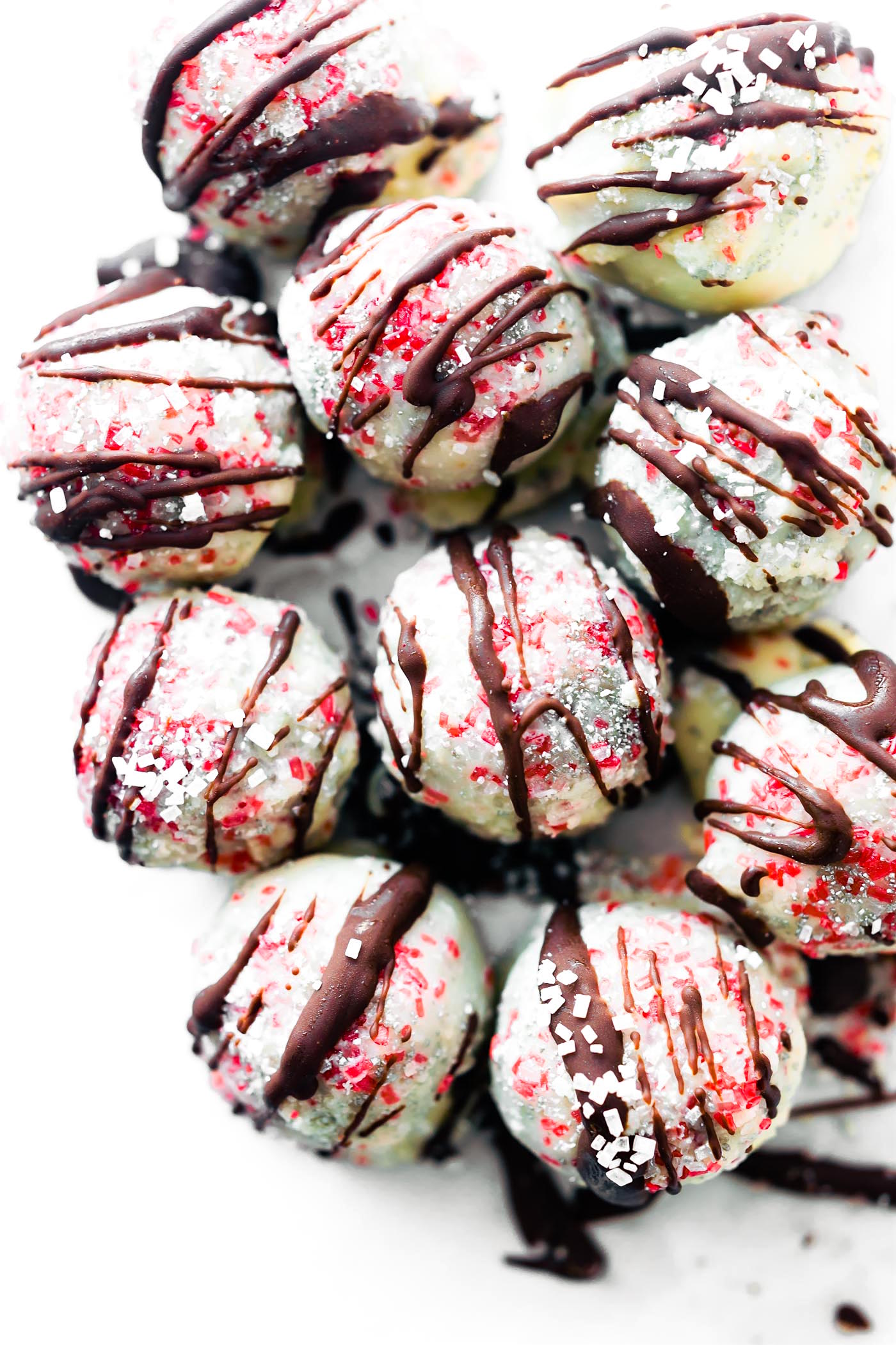 Several white chocolate coated peppermint rum balls with drizzled dark chocolate and red sprinkles.