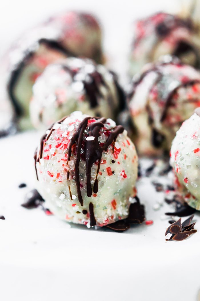 Close up side view of white chocolate peppermint rum balls coated in white chocolate, drizzled with dark chocolate, sprinkled with red sugar crystals.